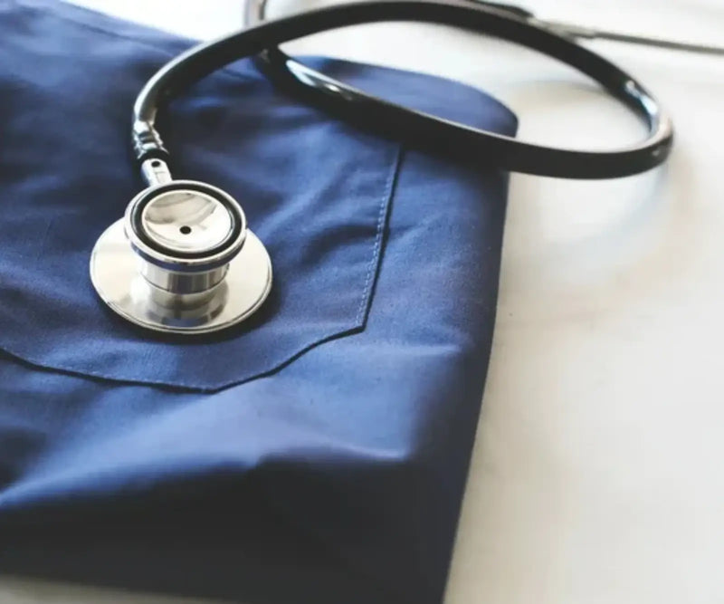 A close-up shot of a black stethoscope with a silver chestpiece resting on a dark blue fabric surface.